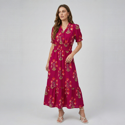 Model posing in a fuchsia floral print tiered maxi dress with v-neck and short sleeves, full-body front view.