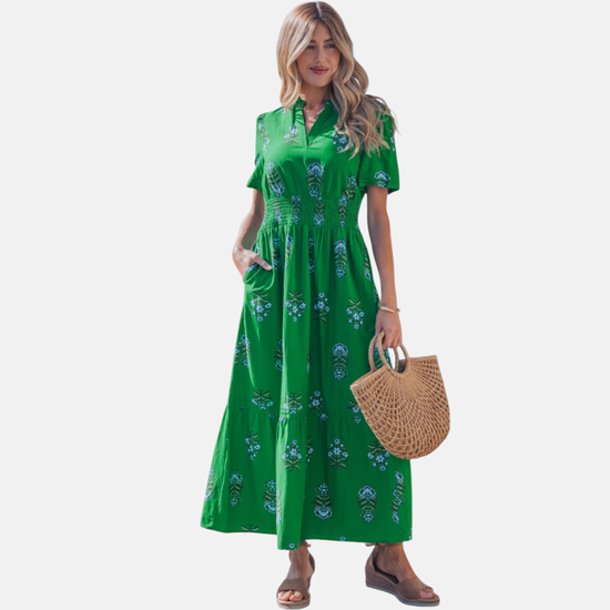 Full-length front view of the green shirred maxi dress, featuring a decorative floral pattern, short sleeves, and a flowing tiered skirt.