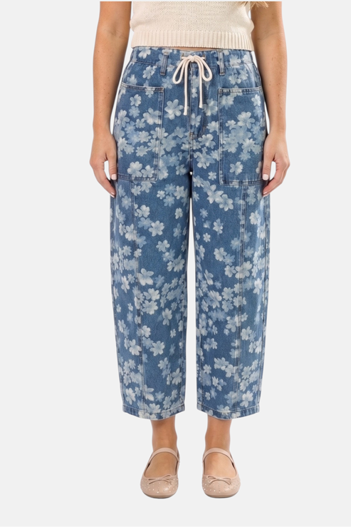 A close-up view of blue floral print barrel jeans featuring a functional cream drawstring waist, large front patch pockets, and a relaxed wide-leg silhouette in a comfortable cotton-blend denim.