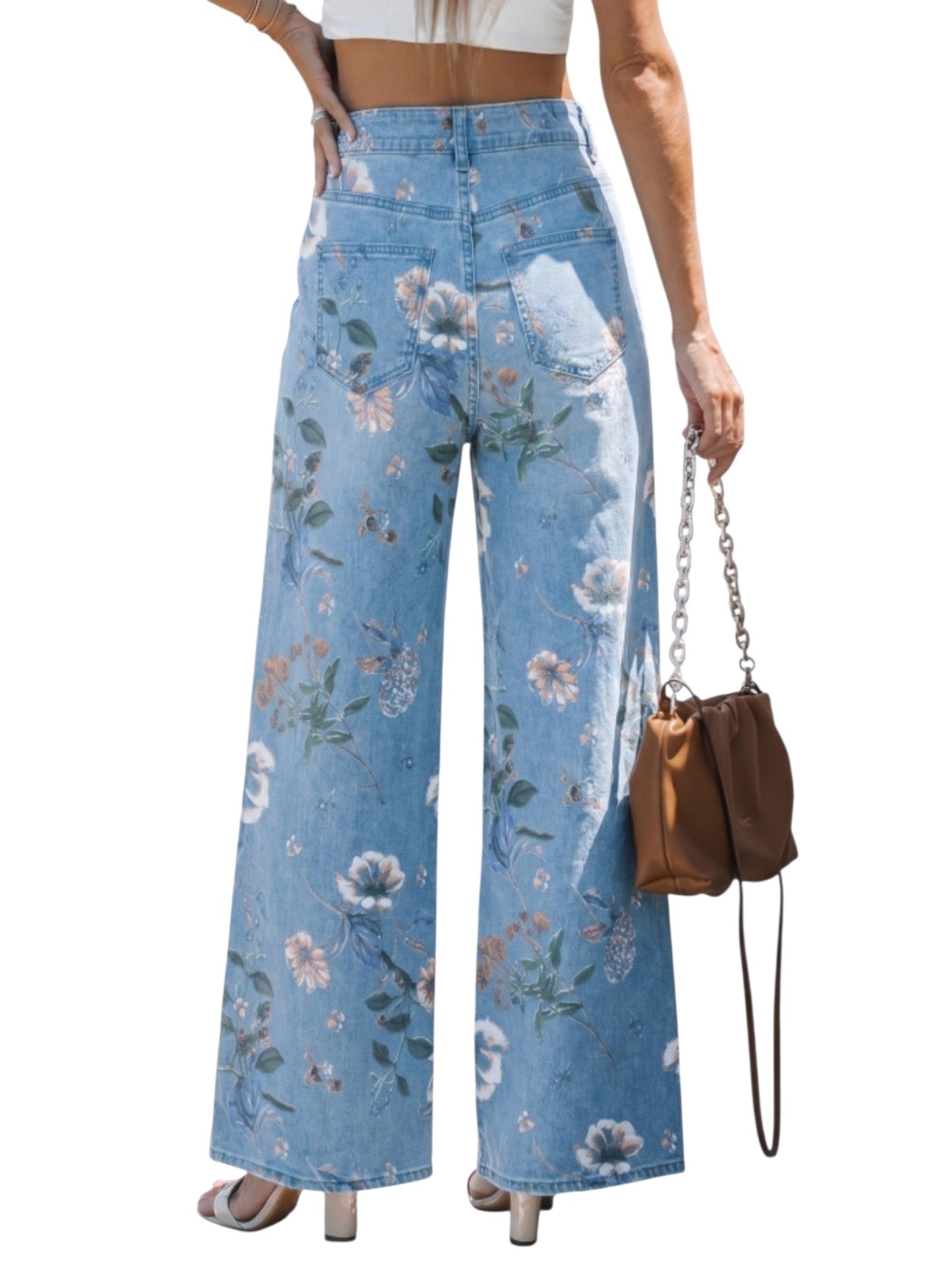 Woman wearing floral-patterned jeans holding a brown handbag on a white background