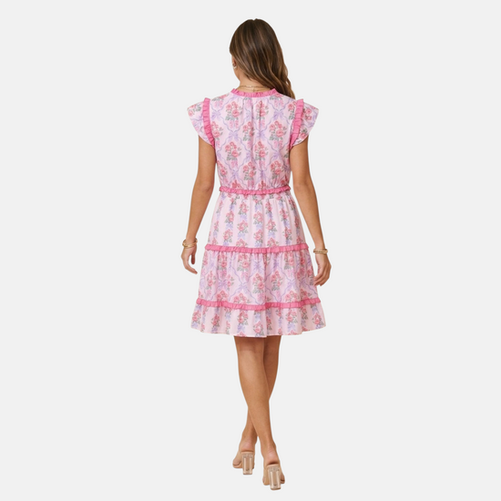Rear view of a model in a pink tiered floral mini dress, highlighting the smocked elastic waist and ruffled skirt layers.
