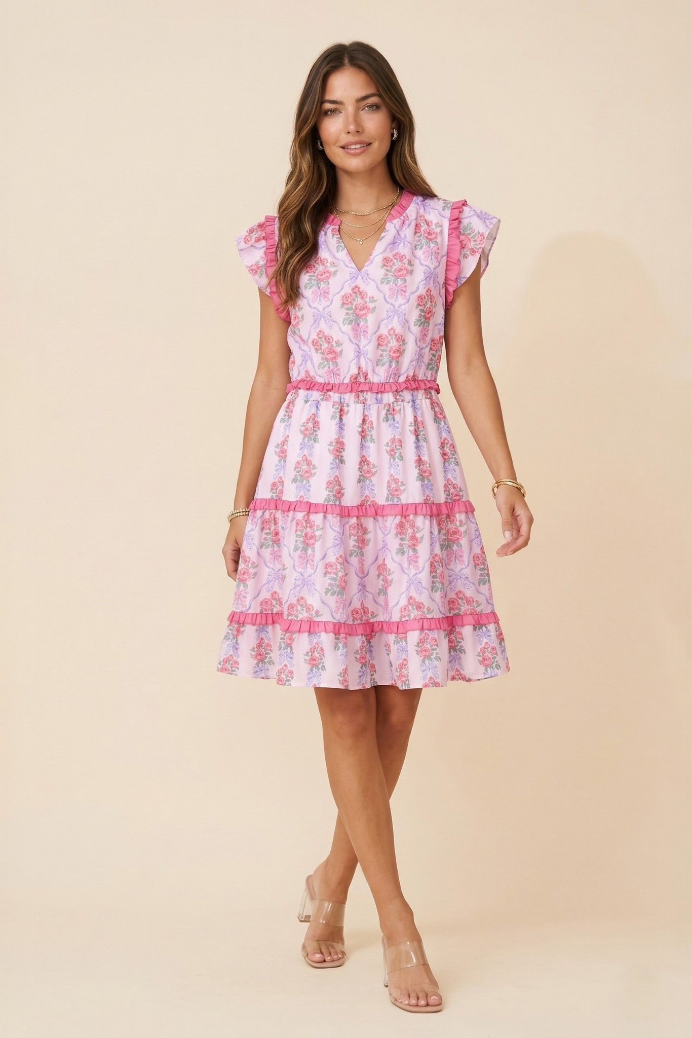 A model showcasing the feminine tiered floral mini dress against a warm beige background, emphasizing its breezy, summer-ready style.