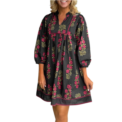 A woman wearing a black 100% cotton mini dress featuring a red floral print, a structured squared yoke with contrast piping, and a notched v-neckline.