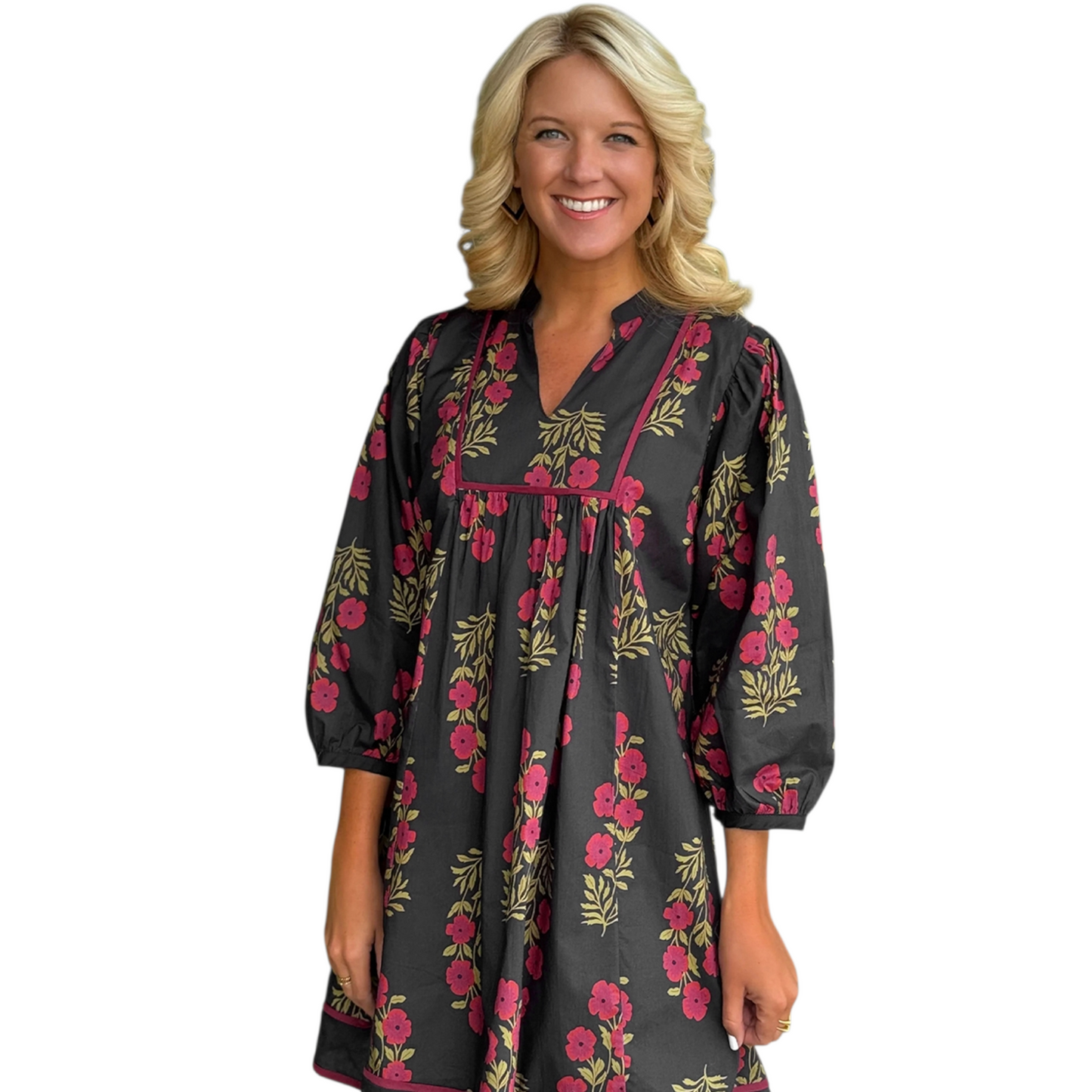 A woman wearing a black 100% cotton mini dress featuring a red floral print, a structured squared yoke with contrast piping, and a notched v-neckline.