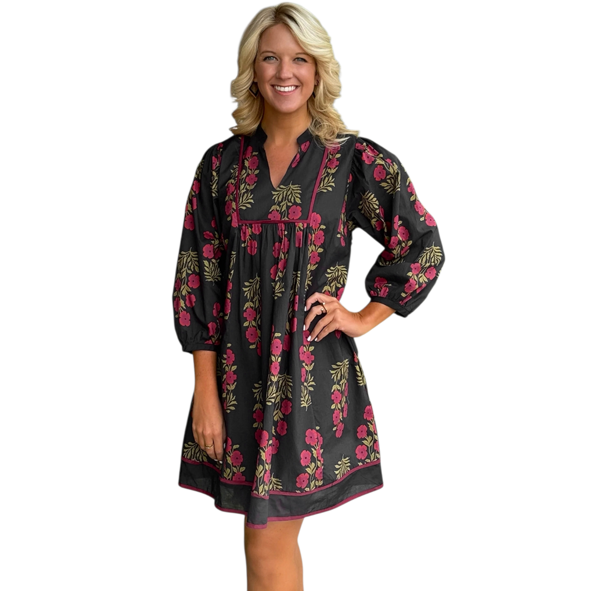 A woman wearing a black 100% cotton mini dress featuring a red floral print, a structured squared yoke with contrast piping, and a notched v-neckline.