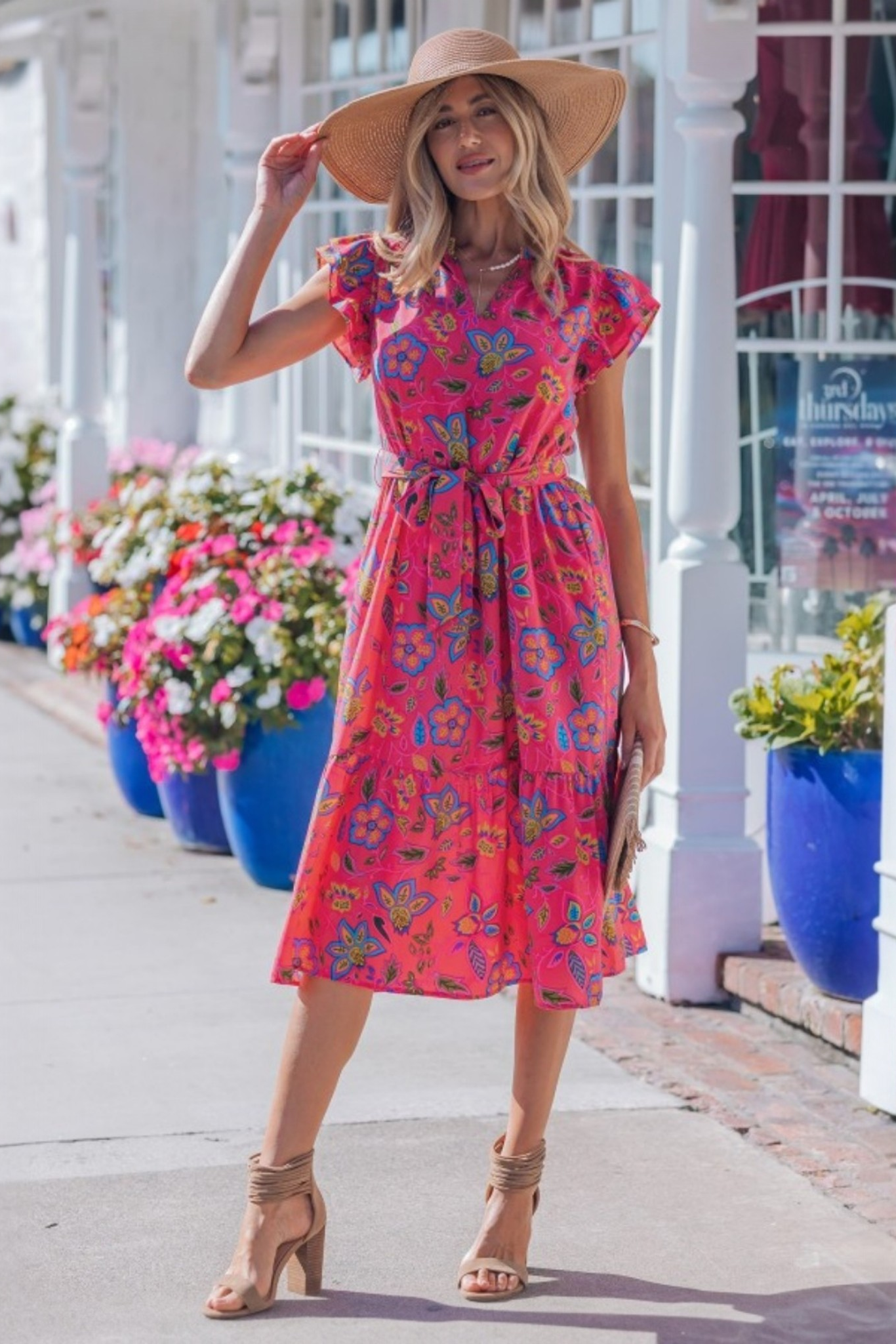 Lifestyle shot of the pink floral flutter-sleeve dress in an outdoor setting, highlighting its vibrant color and "resort-chic" aesthetic.