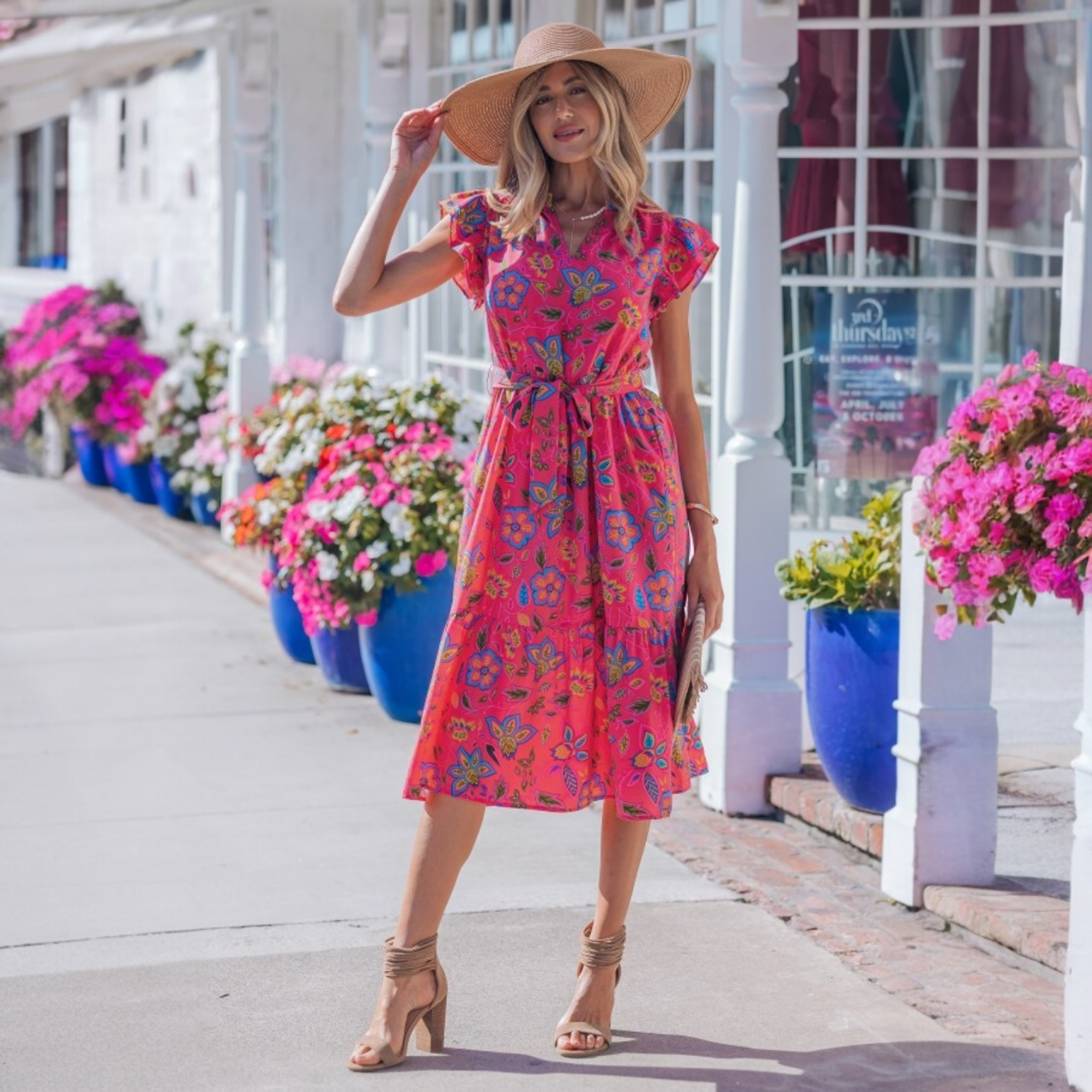 Lifestyle shot of the pink floral flutter-sleeve dress in an outdoor setting, highlighting its vibrant color and "resort-chic" aesthetic.