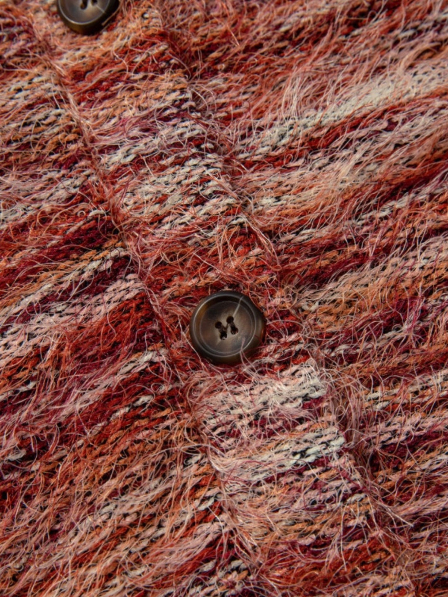Close-up of a textured, fuzzy knit fabric in a marled blend of rust red, orange, brown, and cream, featuring a dark brown button.