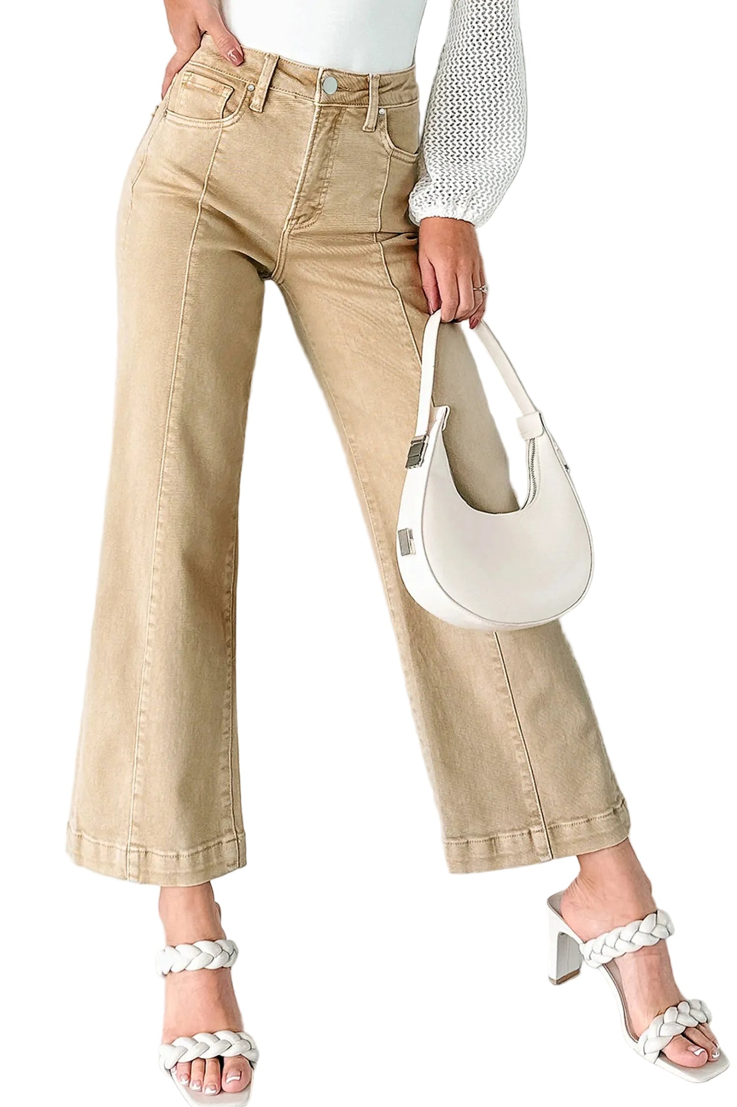 Person wearing beige jeans and white sandals, holding a white handbag against a light background