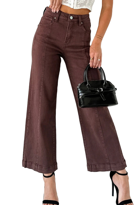 Person wearing brown wide-leg jeans holding a black handbag against a white background