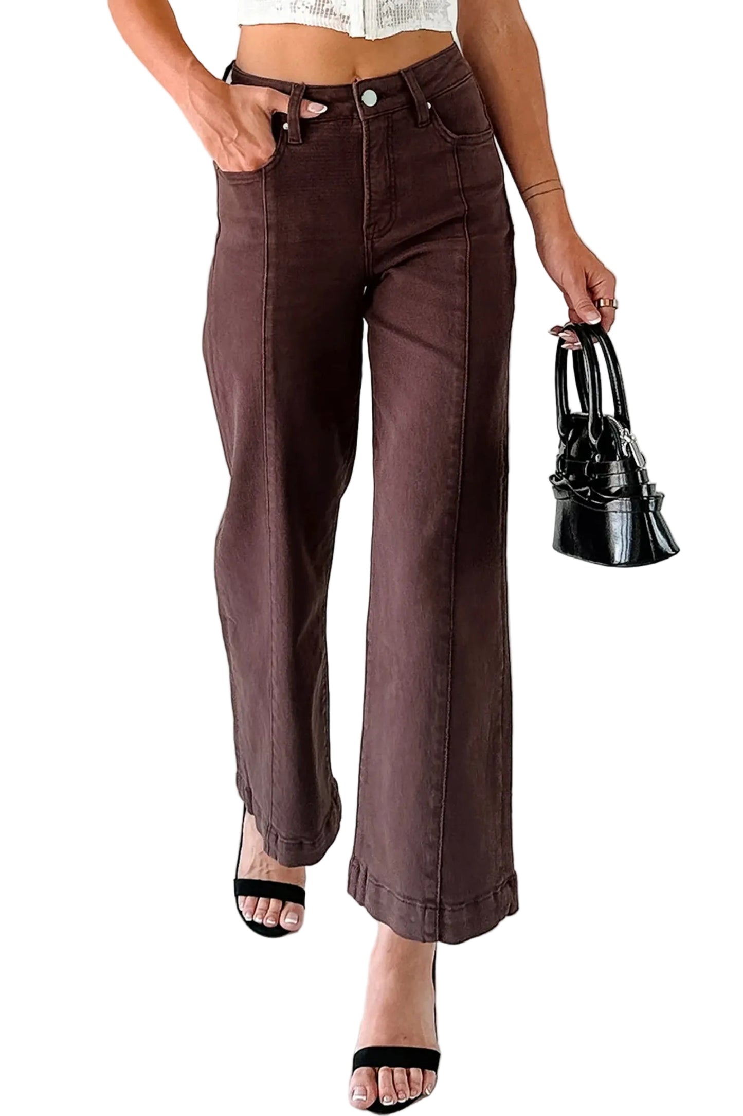 Person wearing brown flared jeans holding a black handbag on a light background