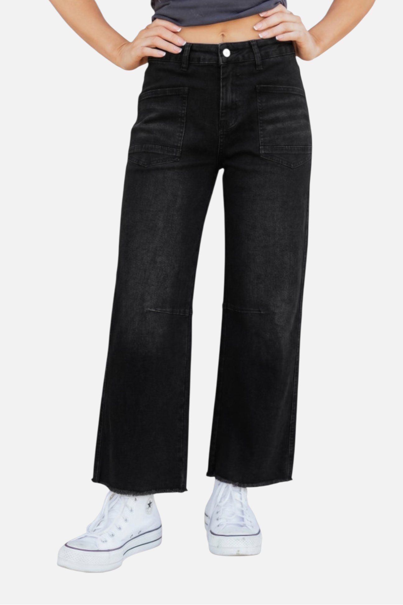 Person wearing black wide-leg jeans and white sneakers on a light gray background