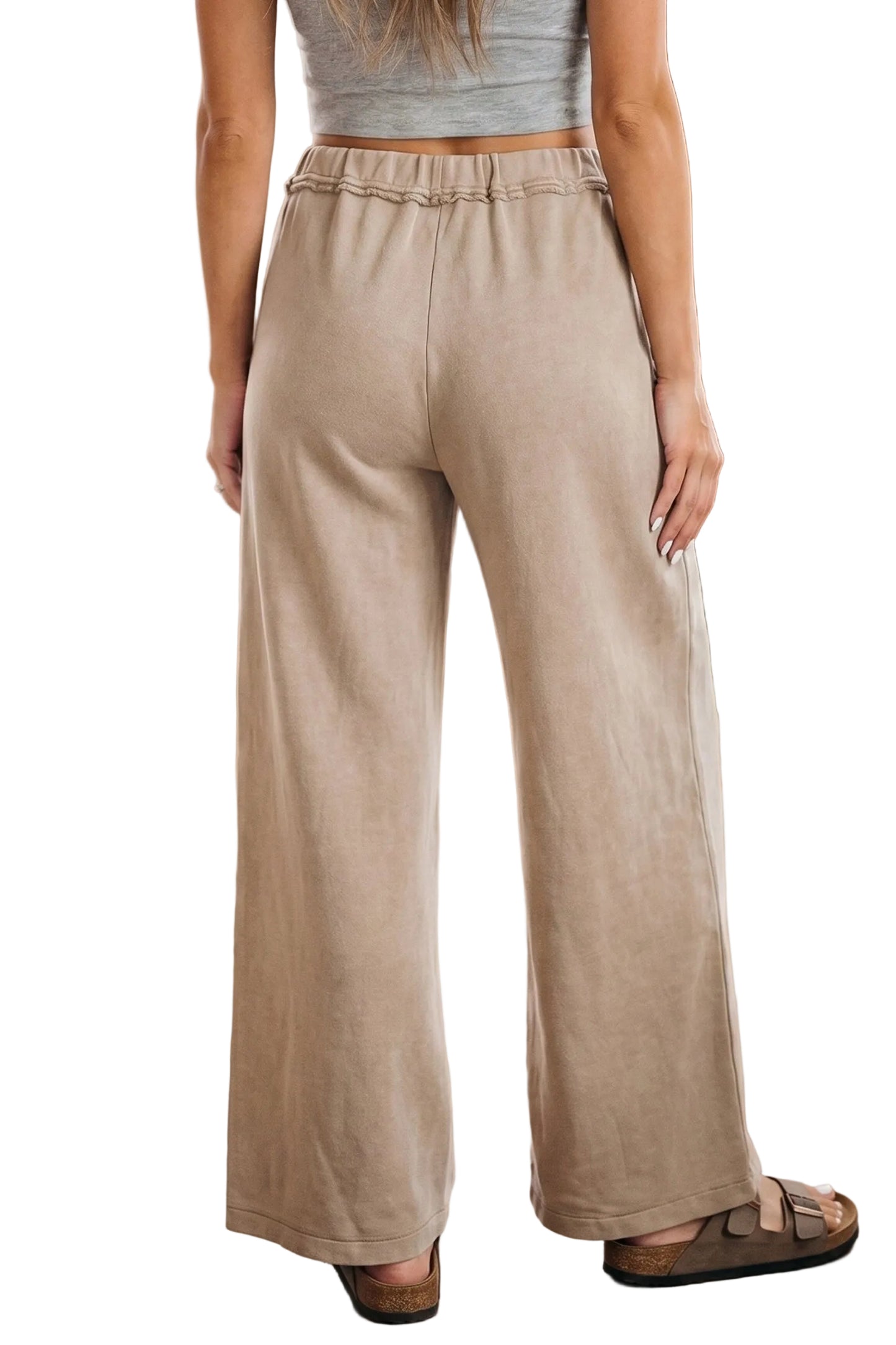 Rear view of the model showcasing the comfortable gathered elastic waistband and smooth drape of the beige cotton trousers.