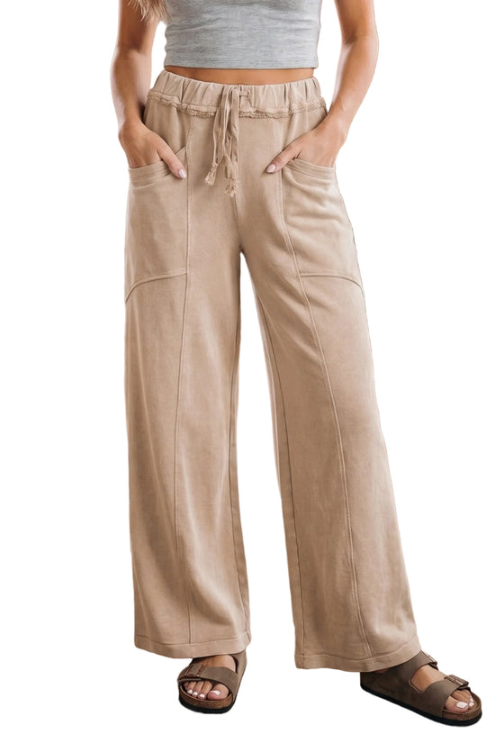 Front view of a model wearing high-waisted beige wide-leg cotton lounge pants with front patch pockets and a drawstring waist.