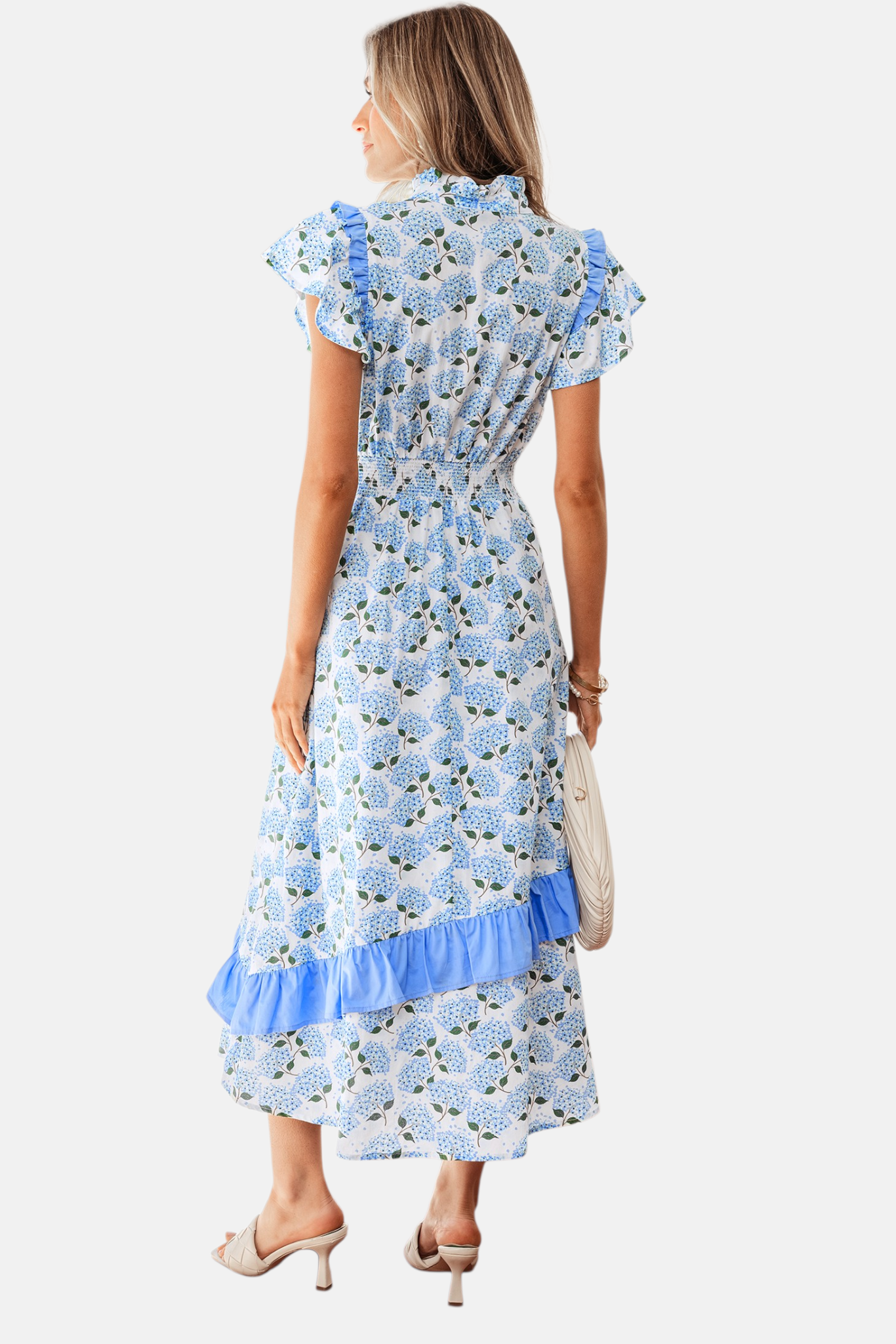 Rear view of a model wearing a hydrangea floral print midi dress featuring a smocked elastic waist and an asymmetric ruffle hem in sky blue.