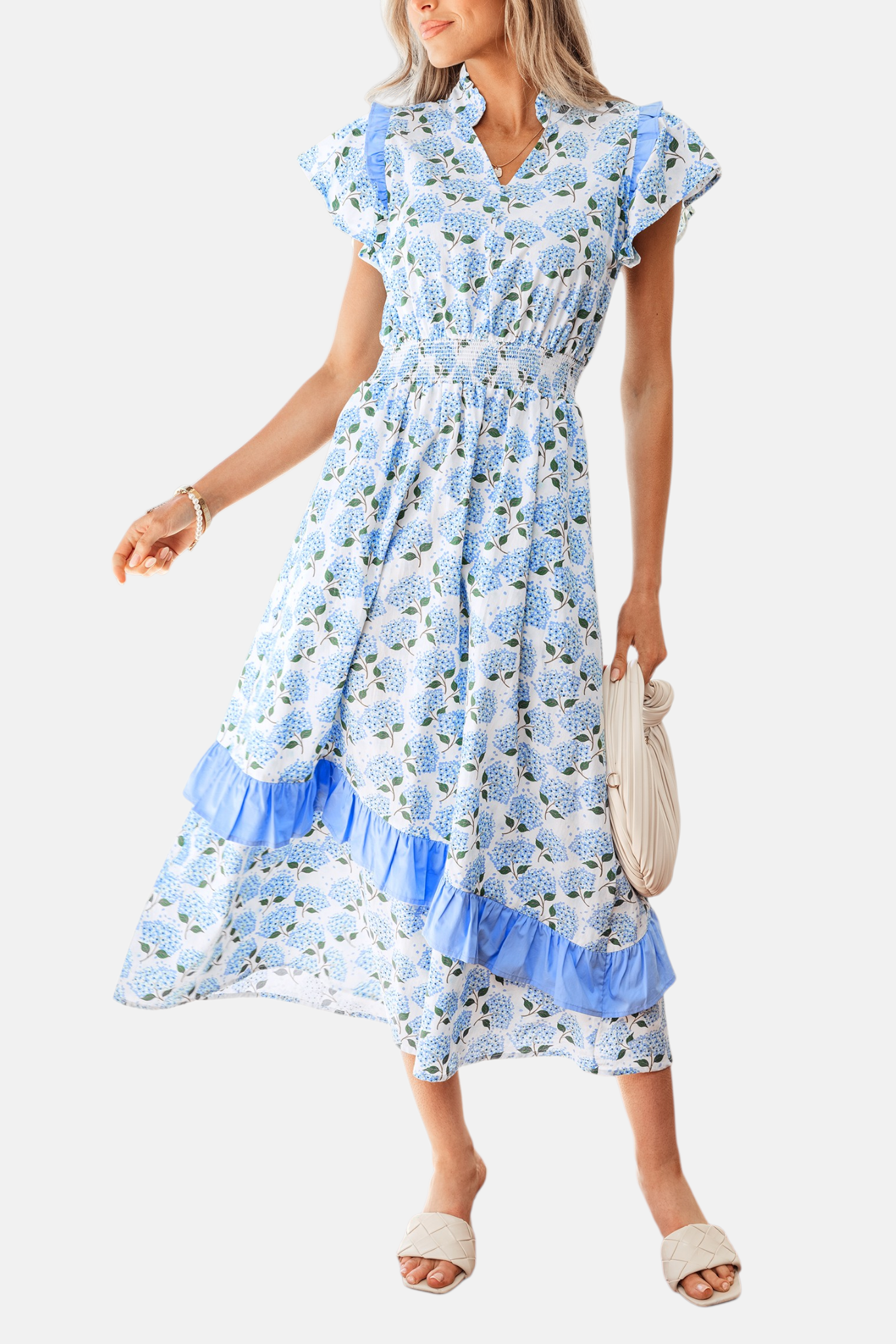 Front view of a white and blue floral midi dress with ruffle cap sleeves and a V-neckline, styled with a white clutch and cream mule heels.