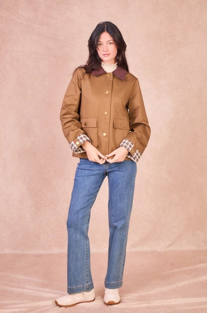 Front view of a model wearing a khaki 100% cotton field jacket with a burgundy corduroy collar and checkered turned-up cuffs.