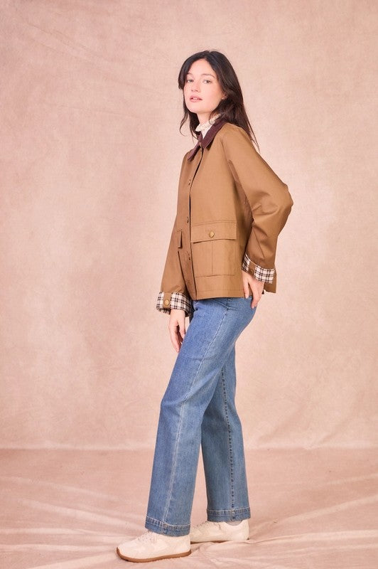 Side view of a model wearing a khaki 100% cotton field jacket with a burgundy corduroy collar and checkered turned-up cuffs.