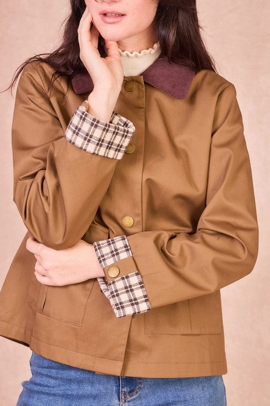Close-up of a khaki cotton jacket highlighting the antique gold button closure, patch pockets, and plaid-lined cuffs.