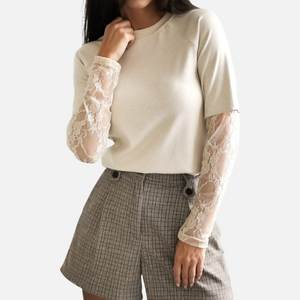 A model wearing a cream-colored top with detailed lace sleeves, paired with plaid shorts, capturing the top's texture and fit.