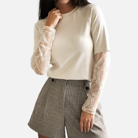 A model wearing a cream-colored top with detailed lace sleeves, paired with plaid shorts, capturing the top's texture and fit.