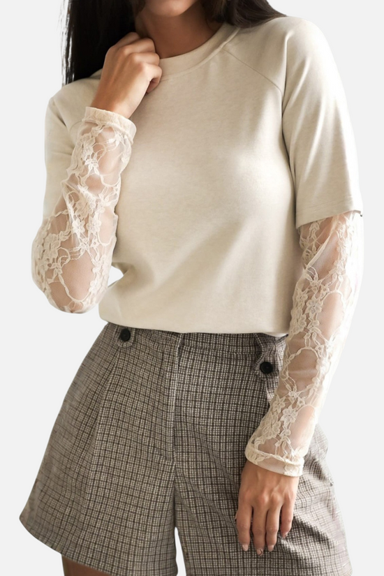 A model wearing a cream-colored top with detailed lace sleeves, paired with plaid shorts, capturing the top's texture and fit.