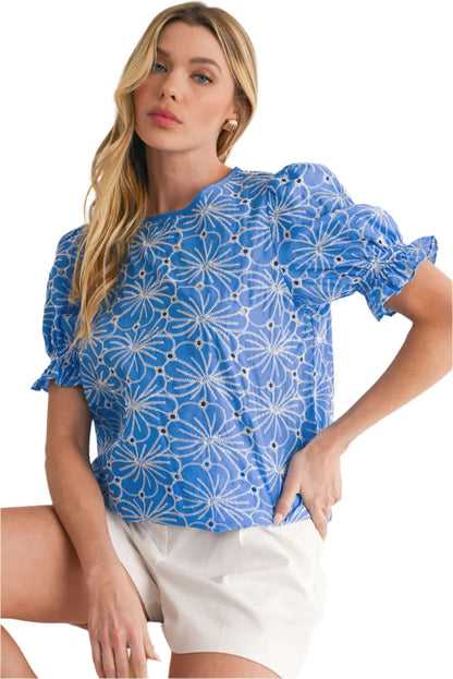 Model wearing a sky blue floral blouse with intricate eyelet accents and frill details.