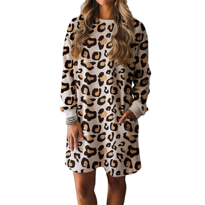 A woman wearing a cream and brown leopard print shift dress with long sleeves, a round neckline, and functional side pockets in a relaxed lifestyle setting.