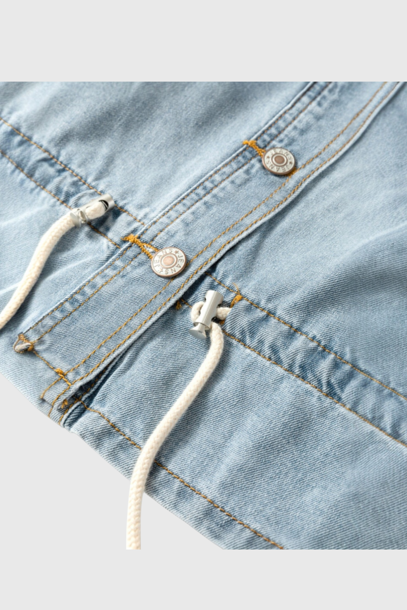 A detailed close-up of the light wash denim jacket hem featuring a functional white cotton drawstring with metallic cord stoppers and branded silver buttons.