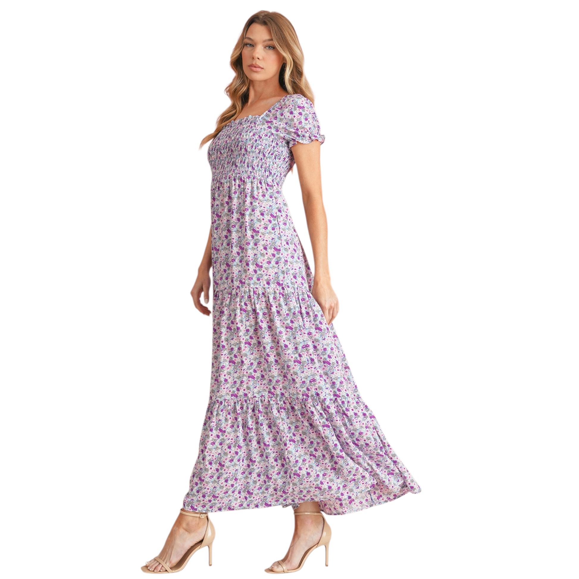 Model wearing a lilac and purple floral smocked maxi dress with short puff sleeves and a tiered skirt. The dress features a square neckline and an elasticated smocked bodice for a flattering fit. Side view.
