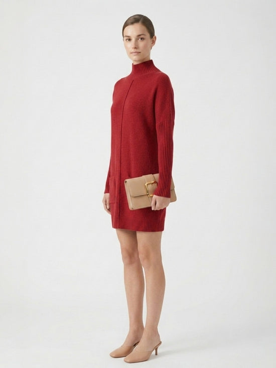 Woman wearing a red sweater dress holding a beige clutch against a white background