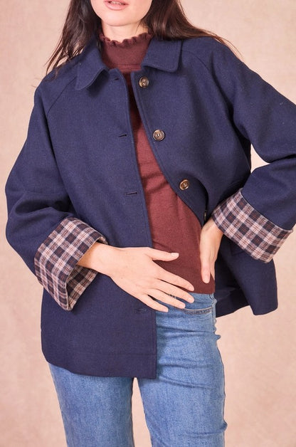 Close-up of the front of a navy jacket highlighting the wool-blend fabric, tortoiseshell-style buttons, and the contrast plaid lining on the sleeve.