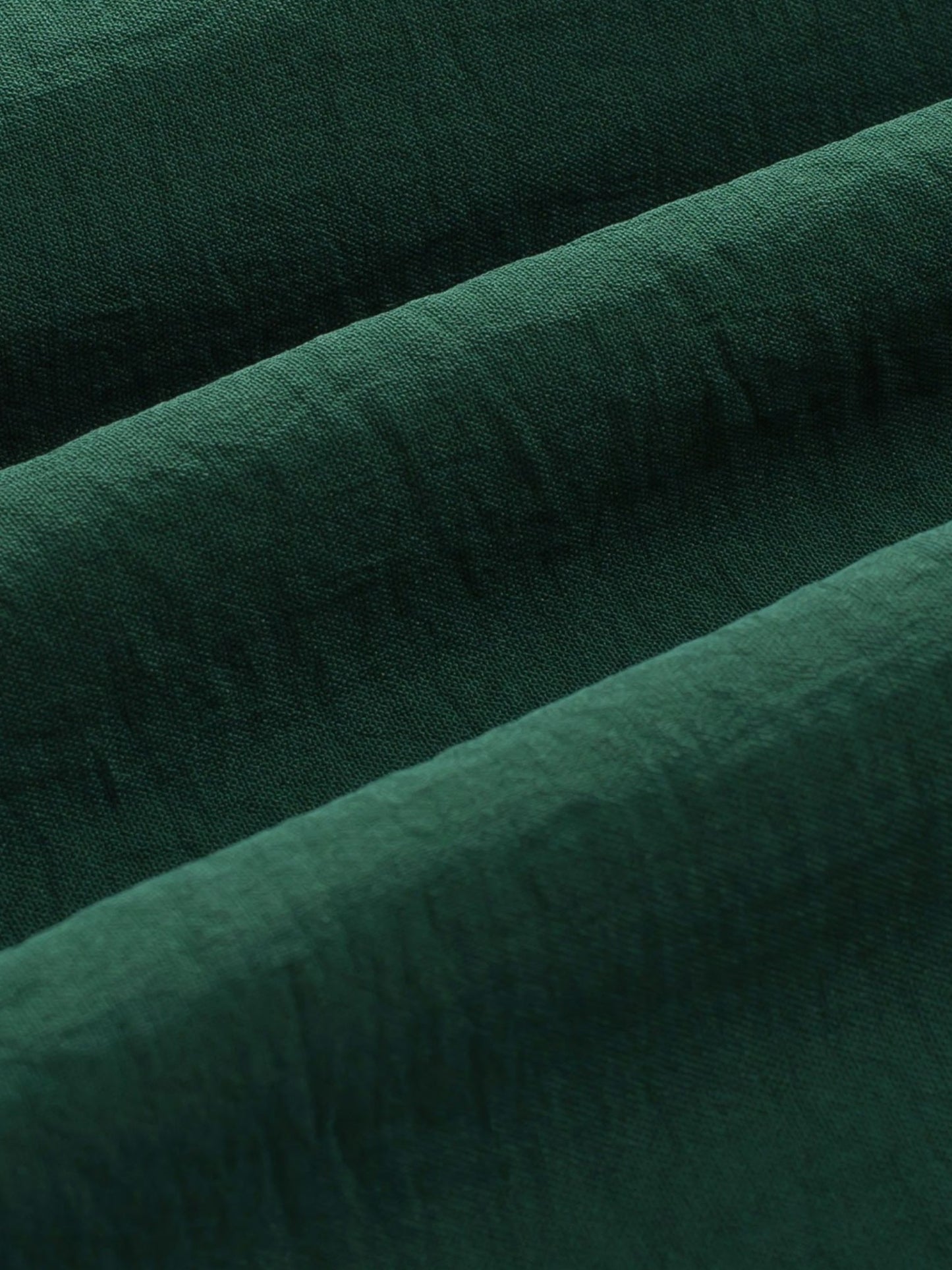A close-up of dark forest green textured fabric with soft diagonal folds.