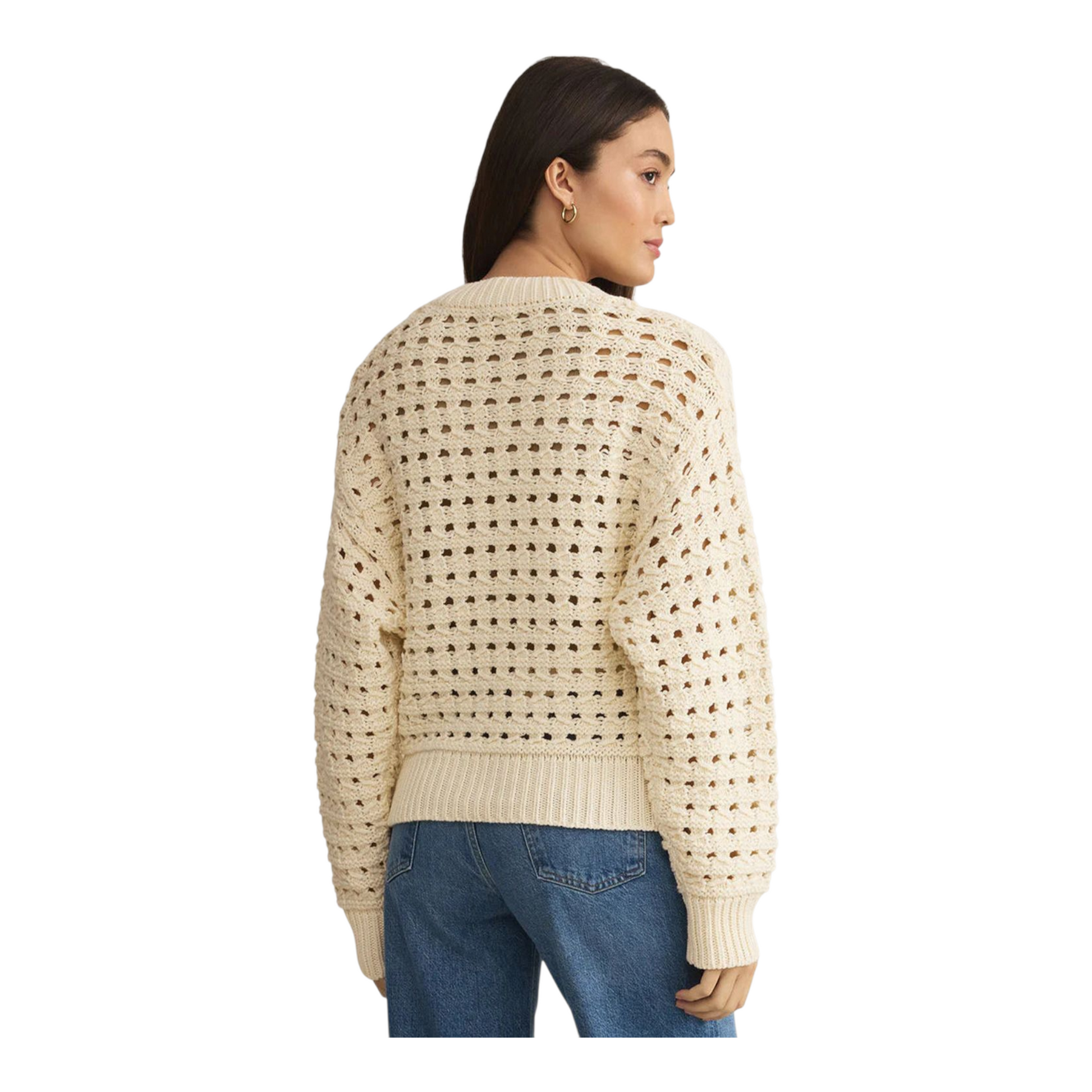 Woman wearing a beige textured sweater and blue jeans on a white background