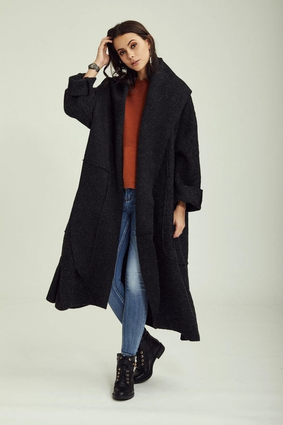 Woman wearing a long black coat over a red sweater and blue jeans on a white background