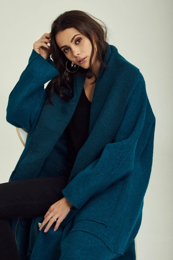 Woman wearing a teal coat against a plain background