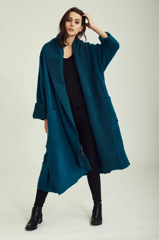 Woman wearing a teal coat on a plain background