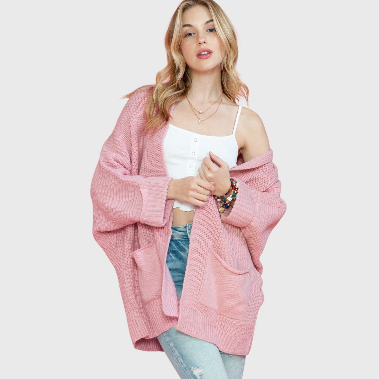A lifestyle shot of a woman wearing an oversized dusty pink open-front cardigan over a white camisole, highlighting the soft knit texture and relaxed fit.