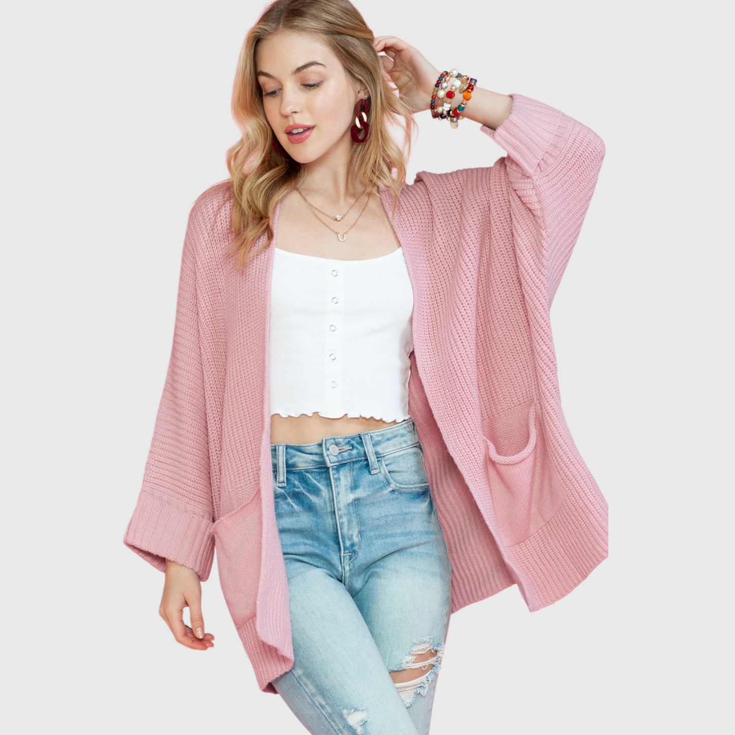 A lifestyle shot of a woman wearing an oversized dusty pink open-front cardigan over a white camisole, highlighting the soft knit texture and relaxed fit.