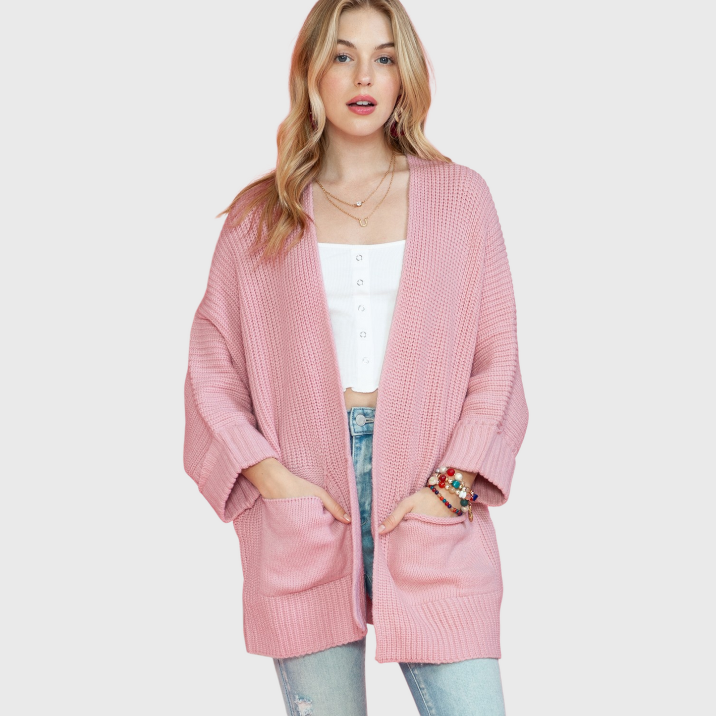 A lifestyle shot of a woman wearing an oversized dusty pink open-front cardigan over a white camisole, highlighting the soft knit texture and relaxed fit.