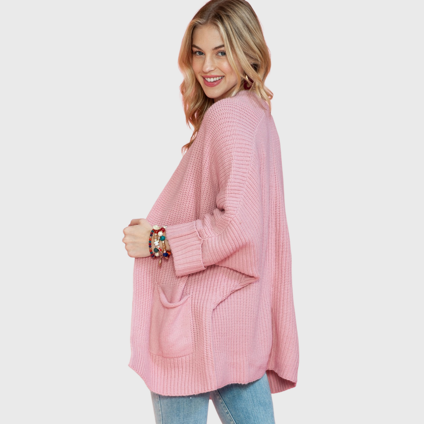 A side-angle view of the pink knit cardigan showcasing the deep knitted patch pockets and the voluminous, slouchy sleeve silhouette.