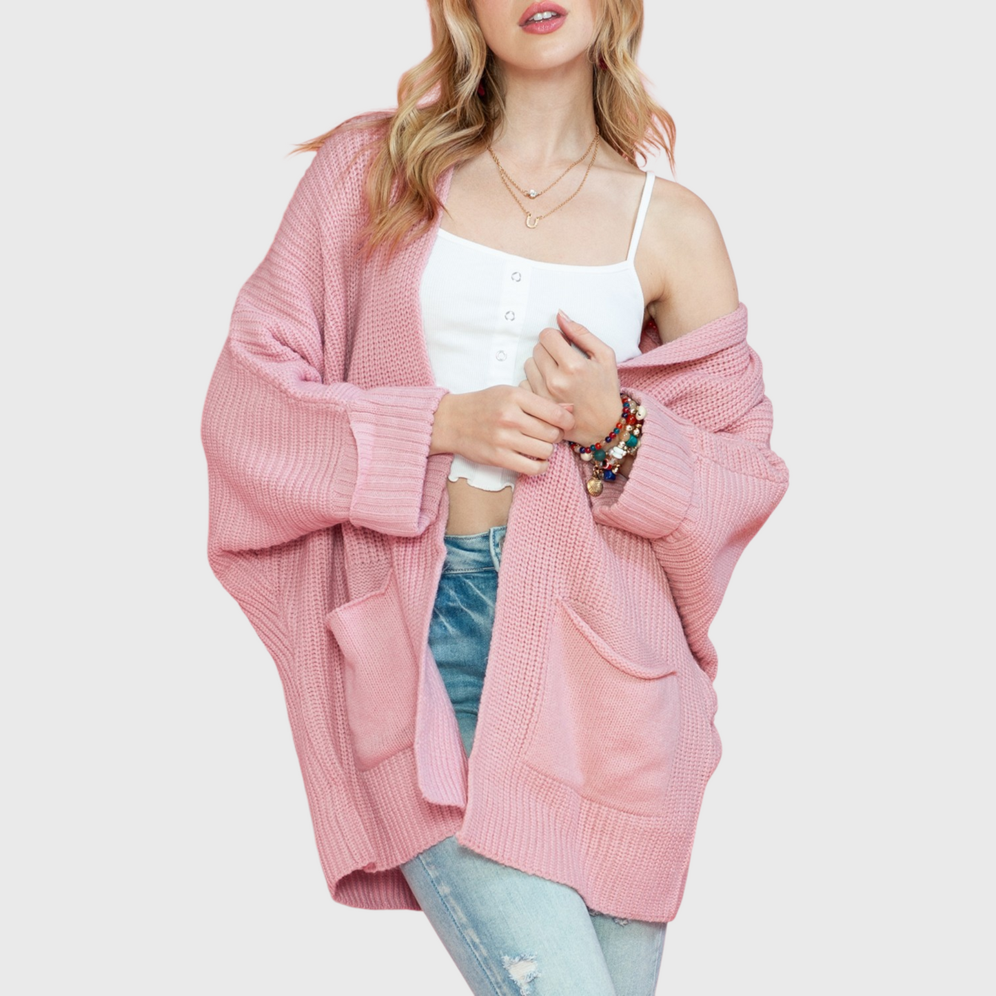 A lifestyle shot of a woman wearing an oversized dusty pink open-front cardigan over a white camisole, highlighting the soft knit texture and relaxed fit.