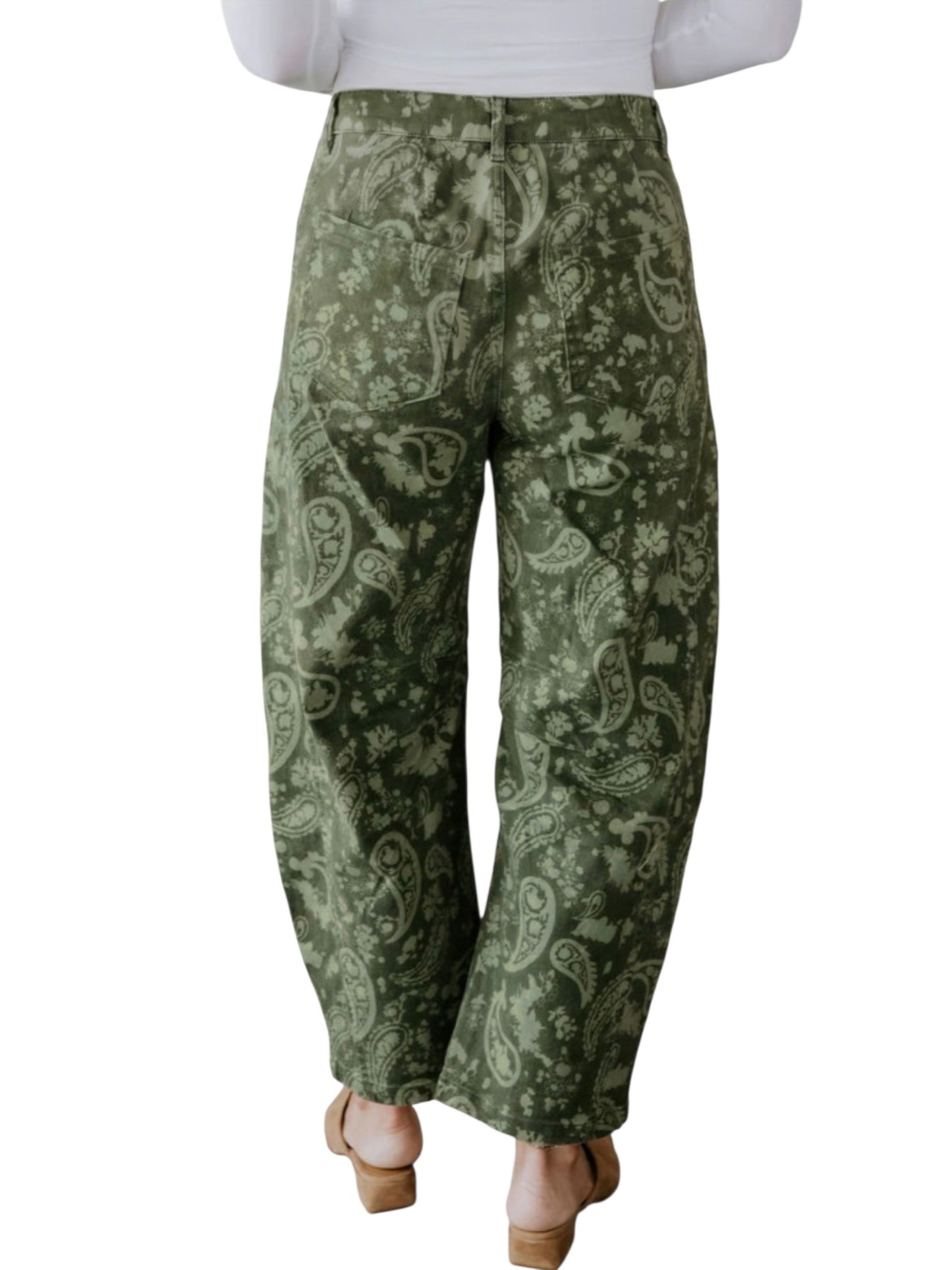 A person shown from the back wearing loose, wide-leg pants with an olive green and light sage paisley pattern, paired with a white top and tan heeled sandals, on a plain white background.
