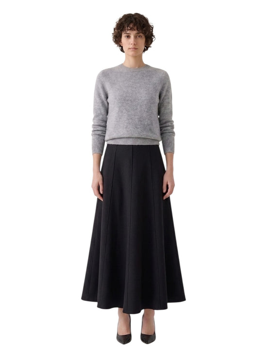 Front full-length view of a model styling a black panelled A-line maxi skirt with a grey crewneck sweater and heels.