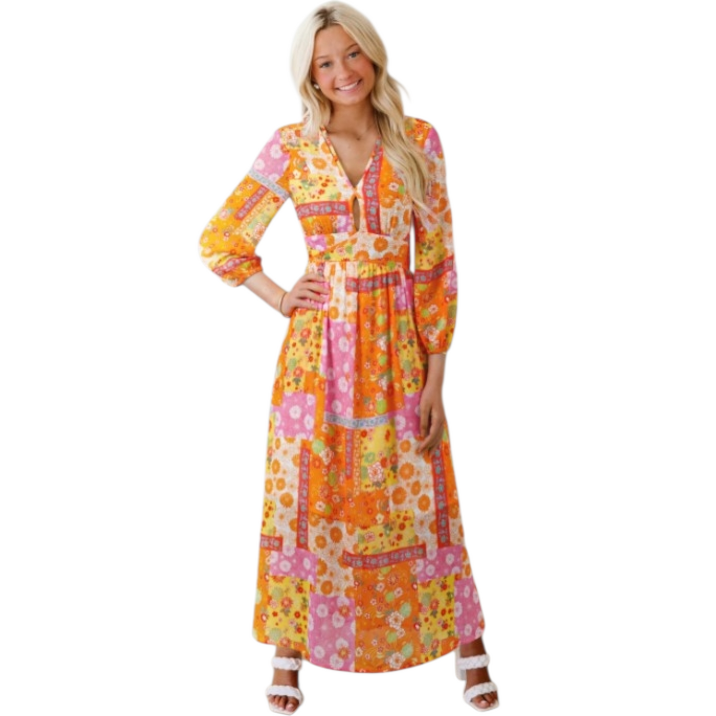 Smiling woman wearing a full-length, long-sleeved maxi dress with a colorful orange, pink, and yellow floral patchwork print and a V-neckline.