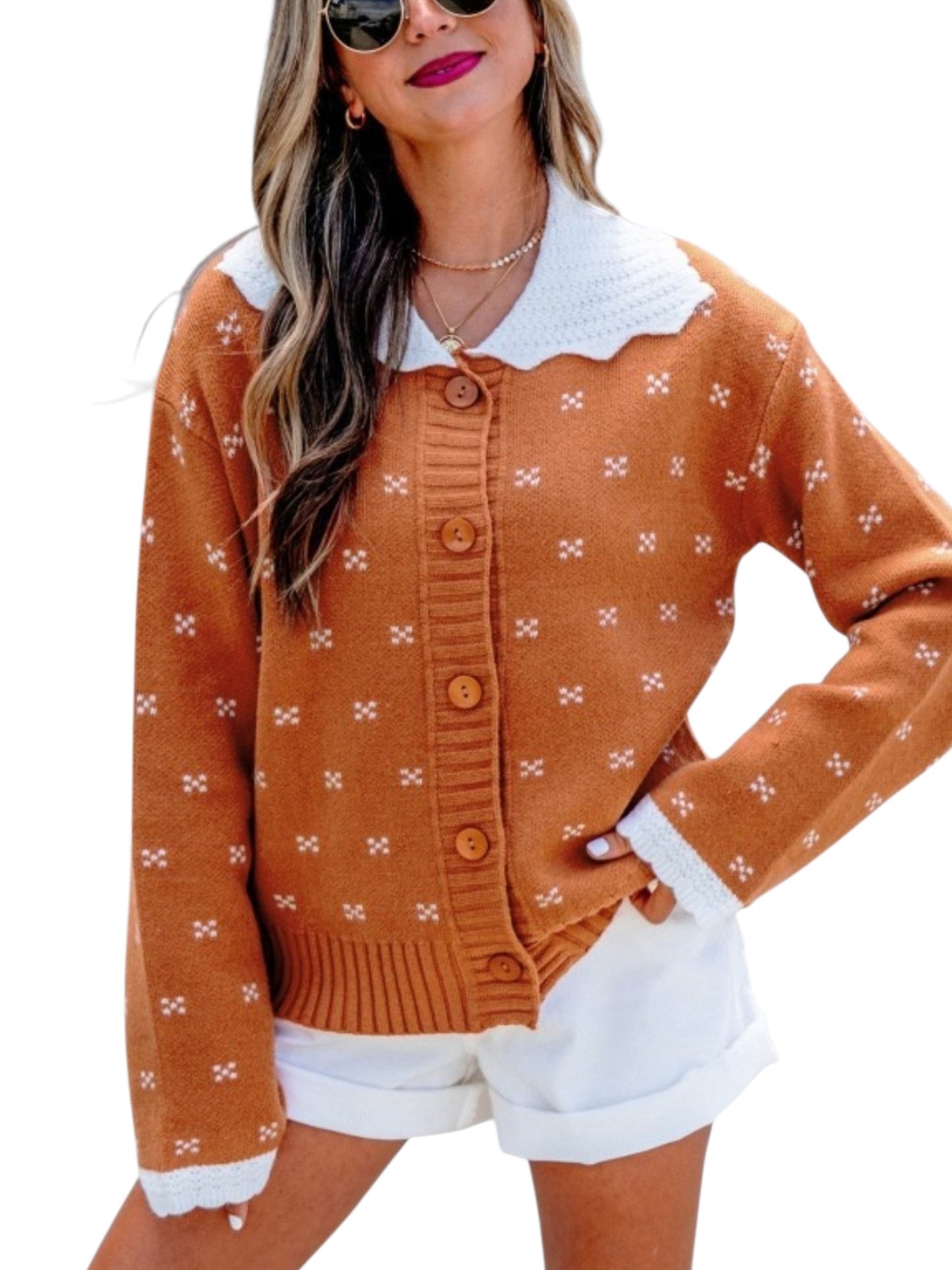 A woman wearing a rust-orange knit cardigan with a white crocheted collar and white cuffs, paired with white shorts, against a plain white background.