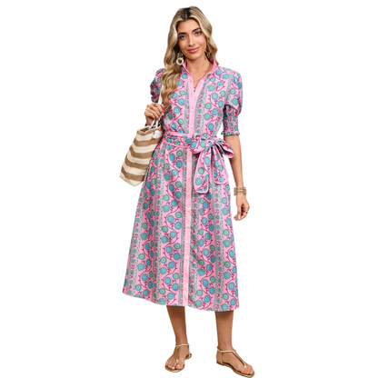 Woman wearing a pink button-down midi dress with a turquoise floral boho print and a matching waist tie belt.