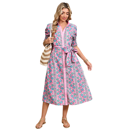 Woman wearing a pink button-down midi dress with a turquoise floral boho print and a matching waist tie belt.