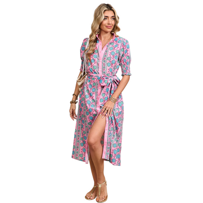 Woman wearing a pink button-down midi dress with a turquoise floral boho print and a matching waist tie belt.