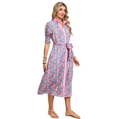 Woman wearing a pink button-down midi dress with a turquoise floral boho print and a matching waist tie belt.